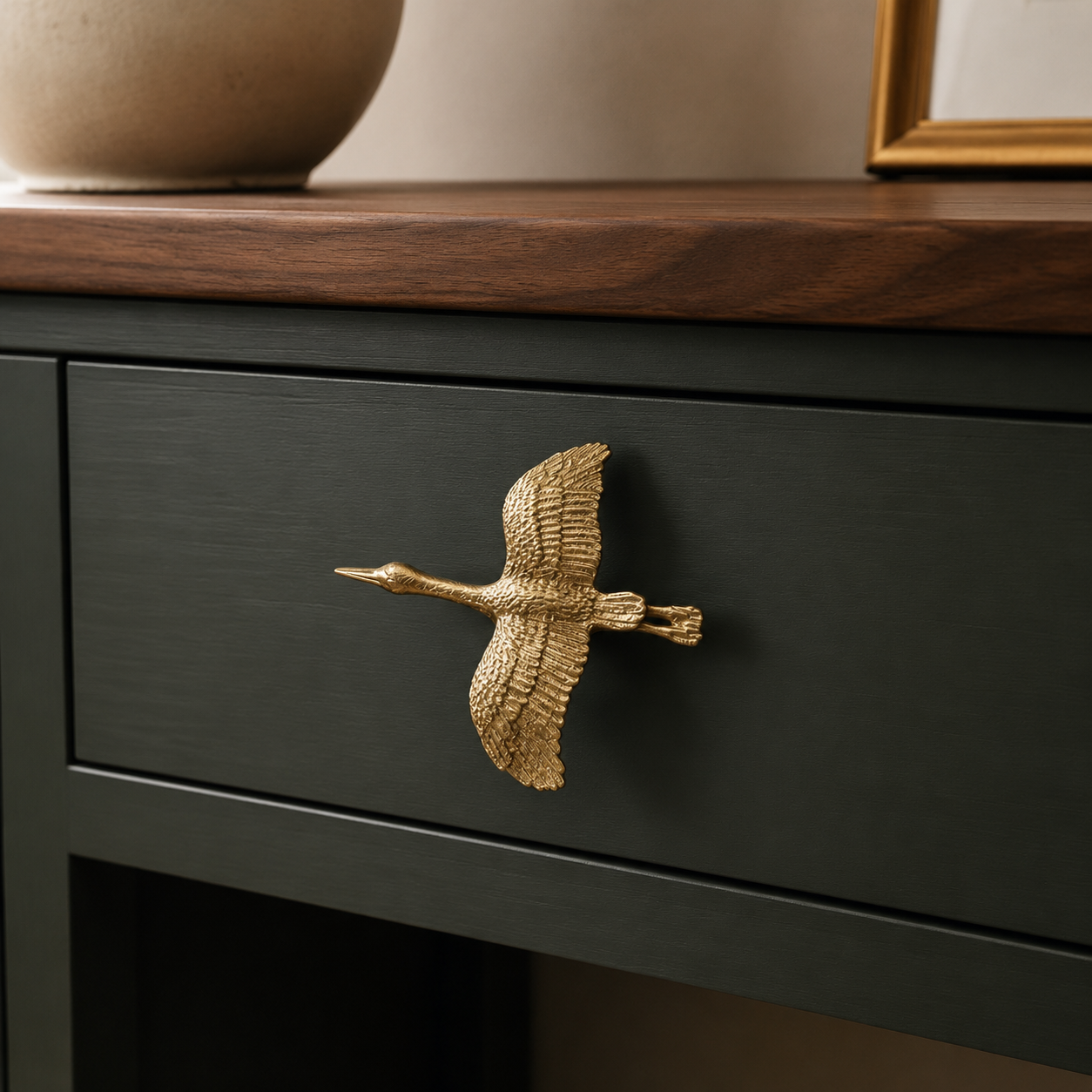 Sculptural brass wild goose pull installed on a dark green cabinet drawer